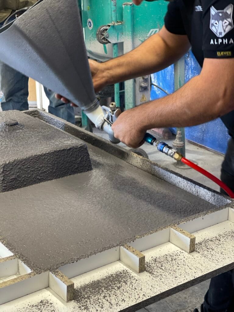 Worker spraying concrete onto formwork with machine.
