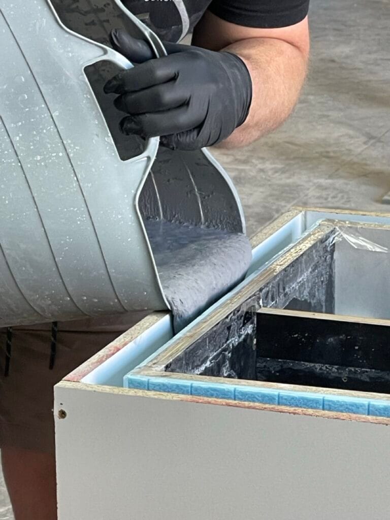 Person pouring concrete into mould with gloves on.