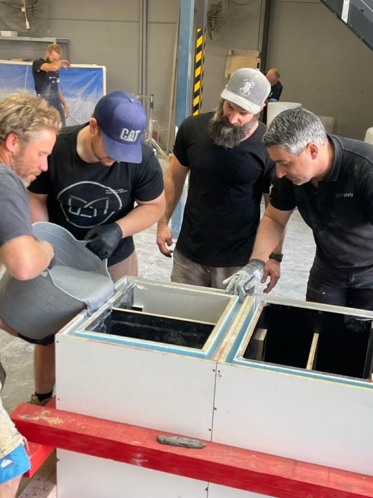 Men pouring concrete into moulds in workshop.