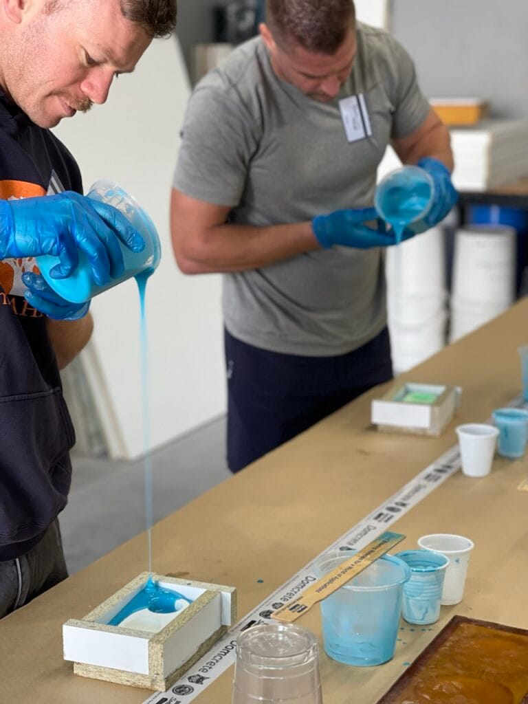 Two men pouring blue resin into moulds.